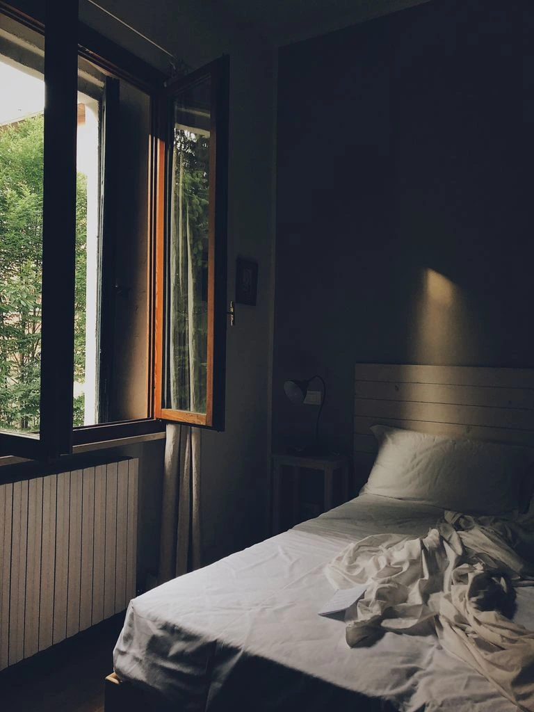 An open book lying face-down on unmade linen sheets in morning light.